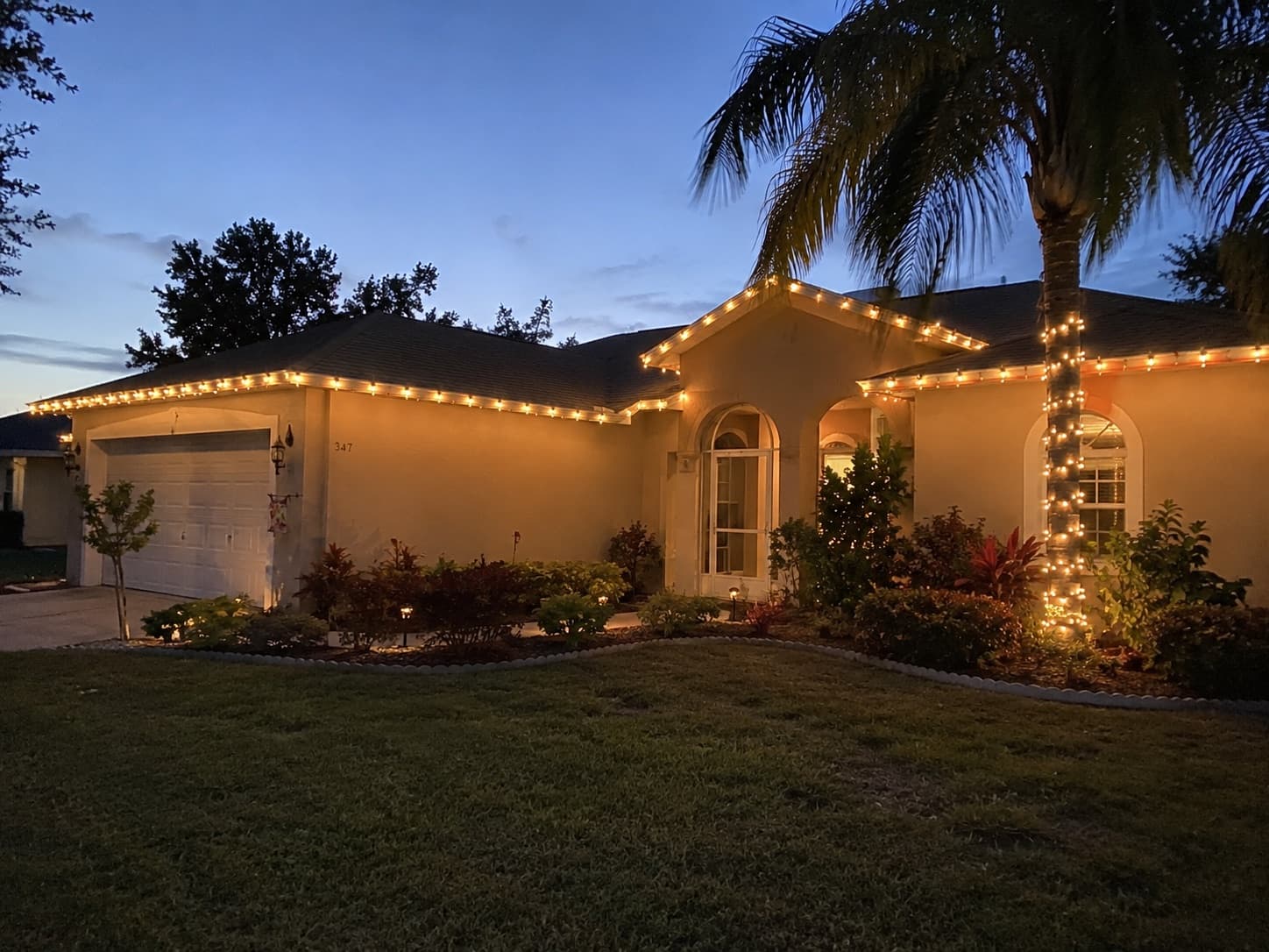 A single-story Florida home at dusk with warm-white holiday lights along the roofline.