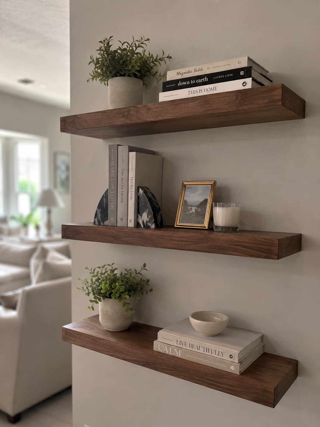 Three wooden floating shelves mounted on a living-room wall with books and decor.